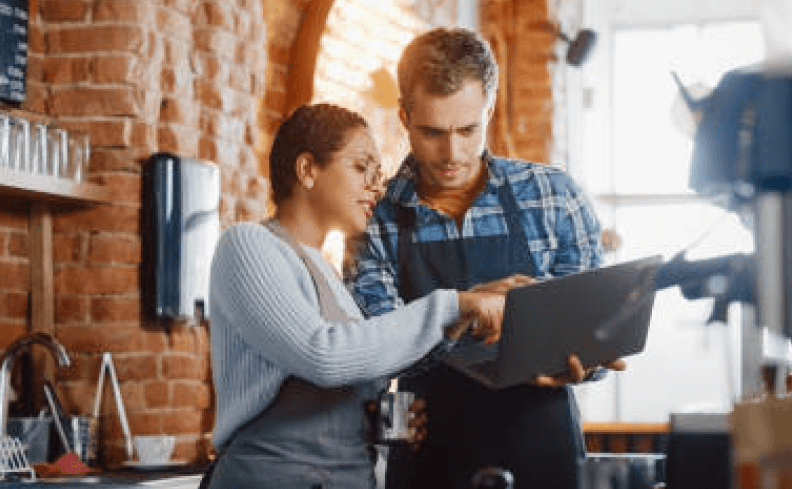Une gérante de restaurant explique à son collaborateur serveur sur un ordinateur comment créer le menu cookie menu